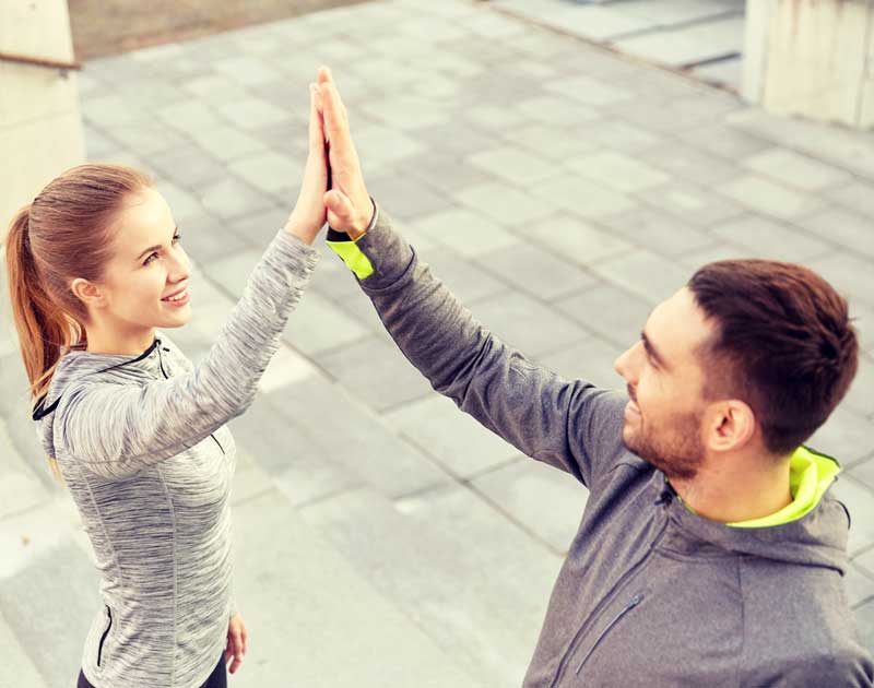 A man and woman wearing athletic gear give each other a high-five outdoors - Chiropractor Langhorne PA A man and woman wearing athletic gear give each other a high-five outdoors - Chiropractor Langhorne PA