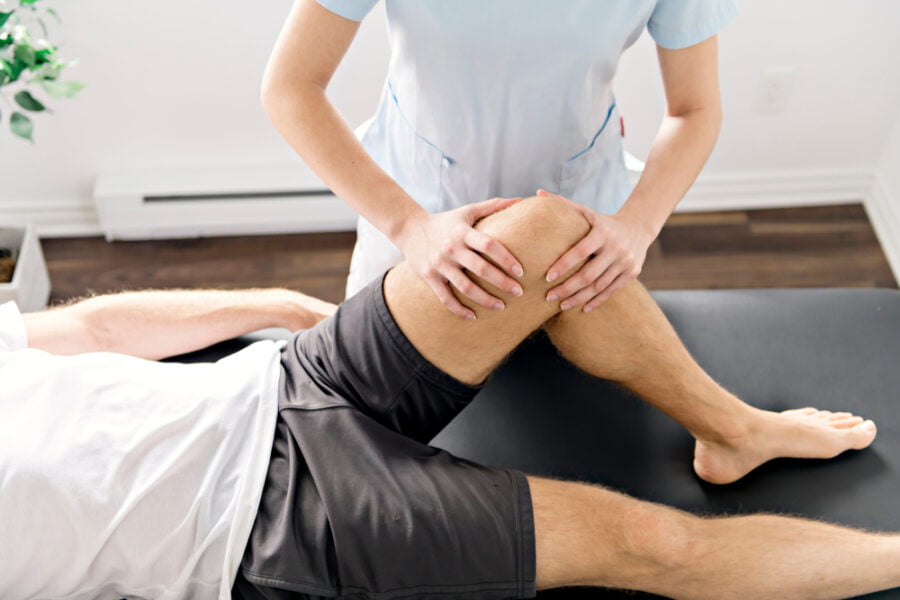 A rehabilitation specialist assisting a patient with manual knee therapy on a treatment table to improve joint function and mobility - Physical Rehabilitation