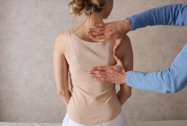 A practitioner evaluating a woman’s spinal alignment and posture by hand as part of a personalized corrective exercise program - Corrective Exercise Programs