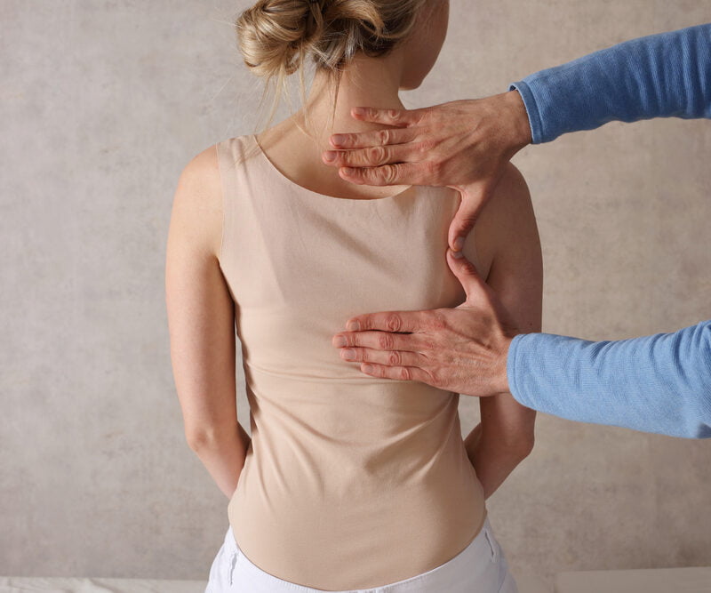A practitioner evaluating a woman’s spinal alignment and posture by hand as part of a personalized corrective exercise program - Corrective Exercise Programs