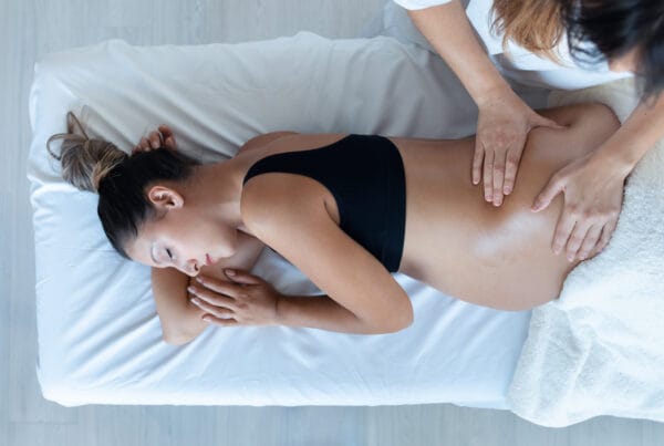 A pregnant woman lying on her side receiving gentle chiropractic adjustments on her lower back to support prenatal wellness - Chiro While Pregnant