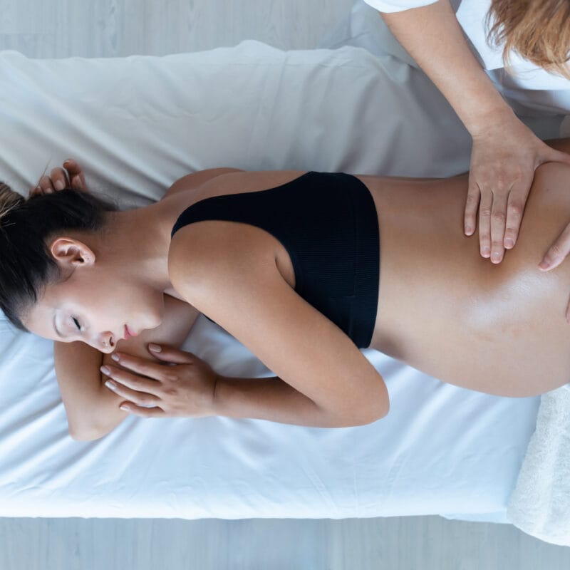 A pregnant woman lying on her side receiving gentle chiropractic adjustments on her lower back to support prenatal wellness - Chiro While Pregnant