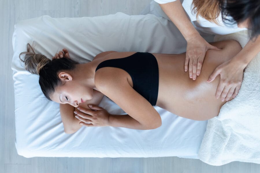A pregnant woman lying on her side receiving gentle chiropractic adjustments on her lower back to support prenatal wellness - Chiro While Pregnant