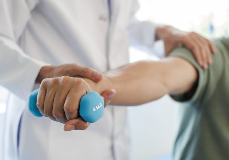 A physical medicine specialist guiding a patient through an arm strengthening exercise using a light blue dumbbell - Physical Medicine and Rehabilitation