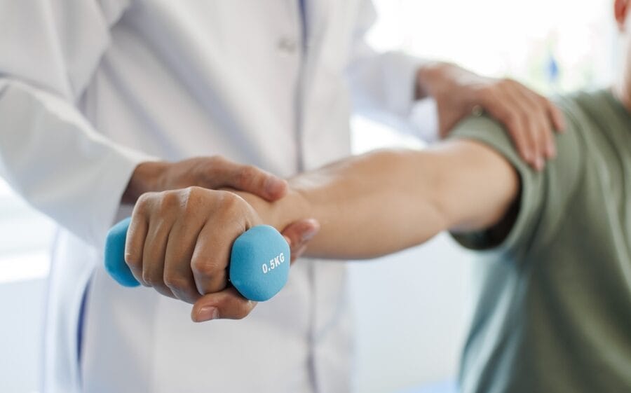 A physical medicine specialist guiding a patient through an arm strengthening exercise using a light blue dumbbell - Physical Medicine and Rehabilitation