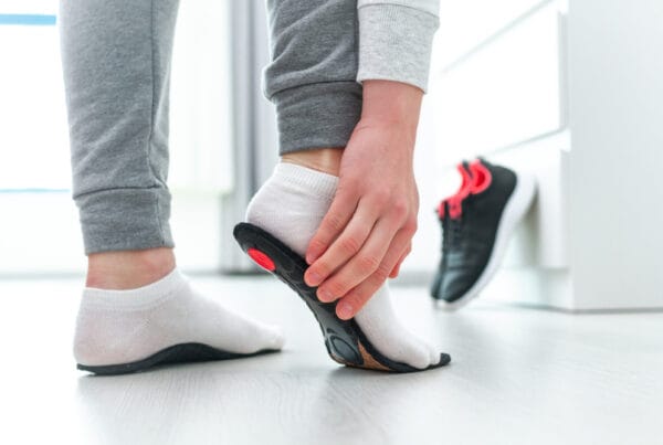 A person wearing white socks inserting a black and red orthotic insole into a running shoe, preparing for foot support - Orthotics