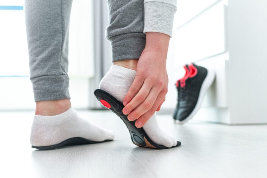 A person wearing white socks inserting a black and red orthotic insole into a running shoe, preparing for foot support - Orthotics
